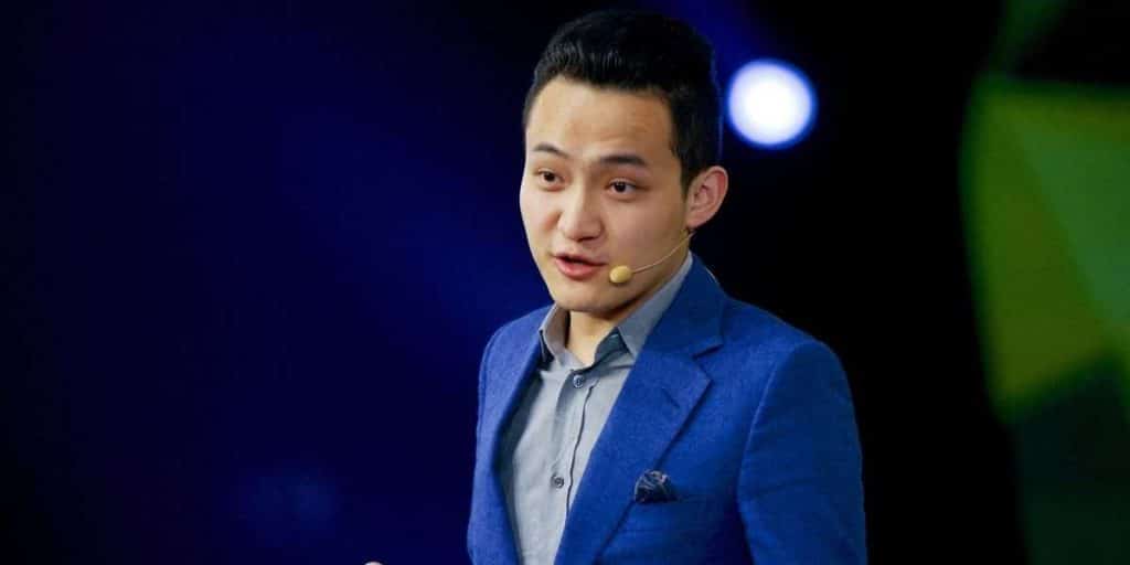 Man in blue suit speaking on stage with a headset microphone.