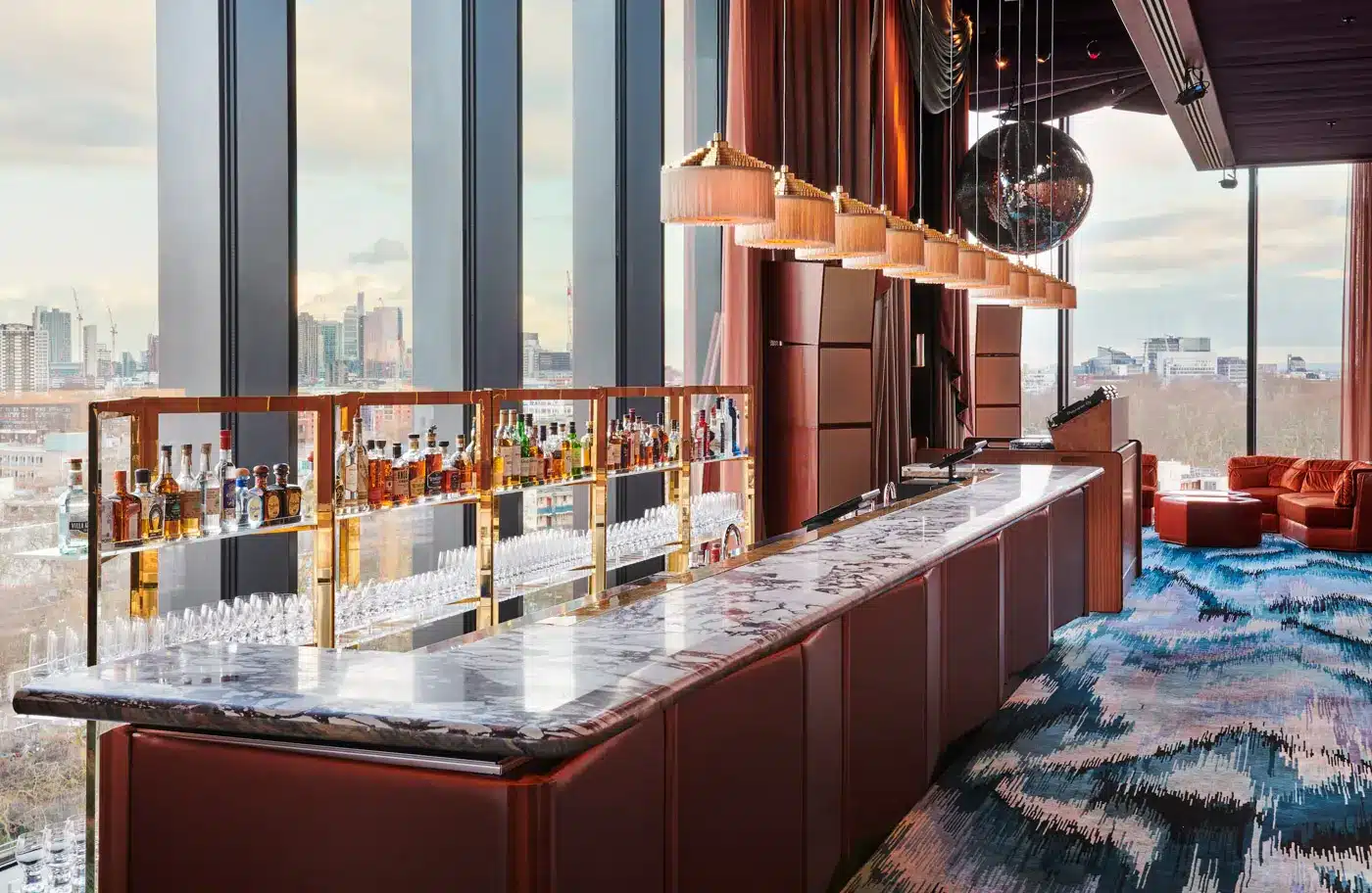 Elegant bar interior with marble top, shelves of liquor, and city view through large windows.