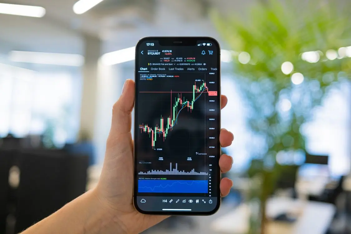 A smartphone displaying a Bitcoin trading chart with green and red candlesticks.