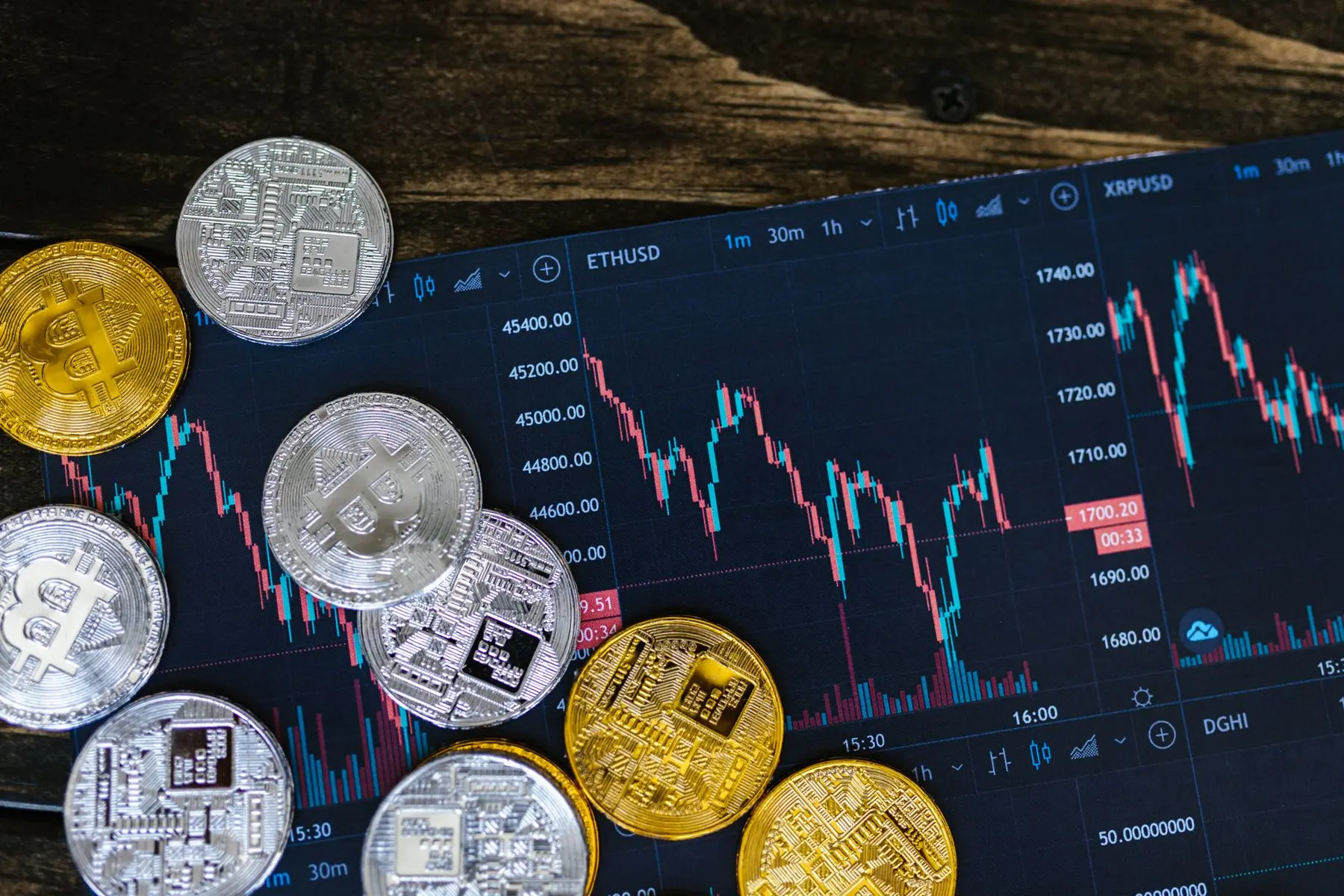 Gold and silver Bitcoin coins resting on a digital screen displaying cryptocurrency trading charts