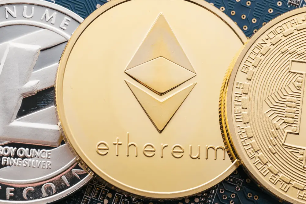 Close-up of a gold Ethereum coin with the logo and name, flanked by Bitcoin and other cryptocurrency coins on a circuit board.