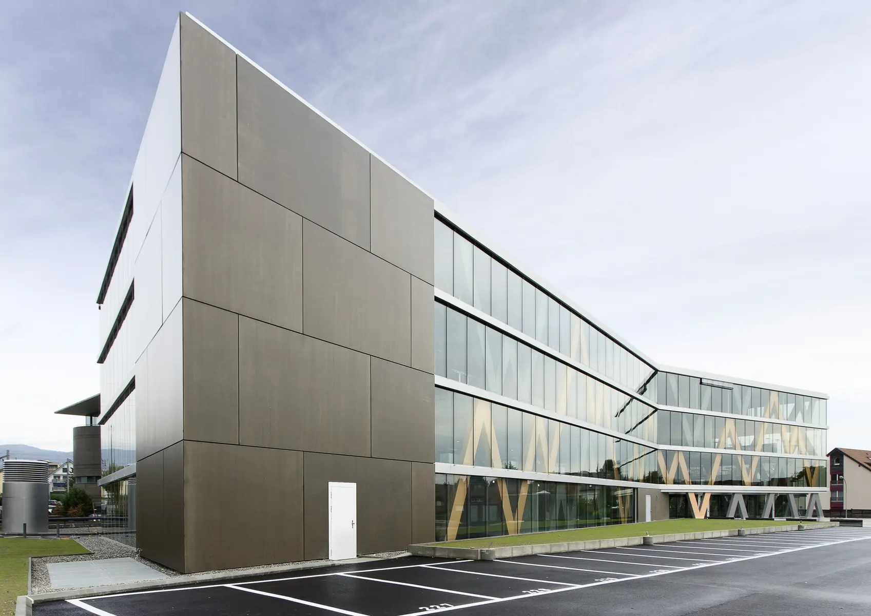 Modern architectural view of the Swissquote headquarters building in Gland featuring a grey facade and glass walls.