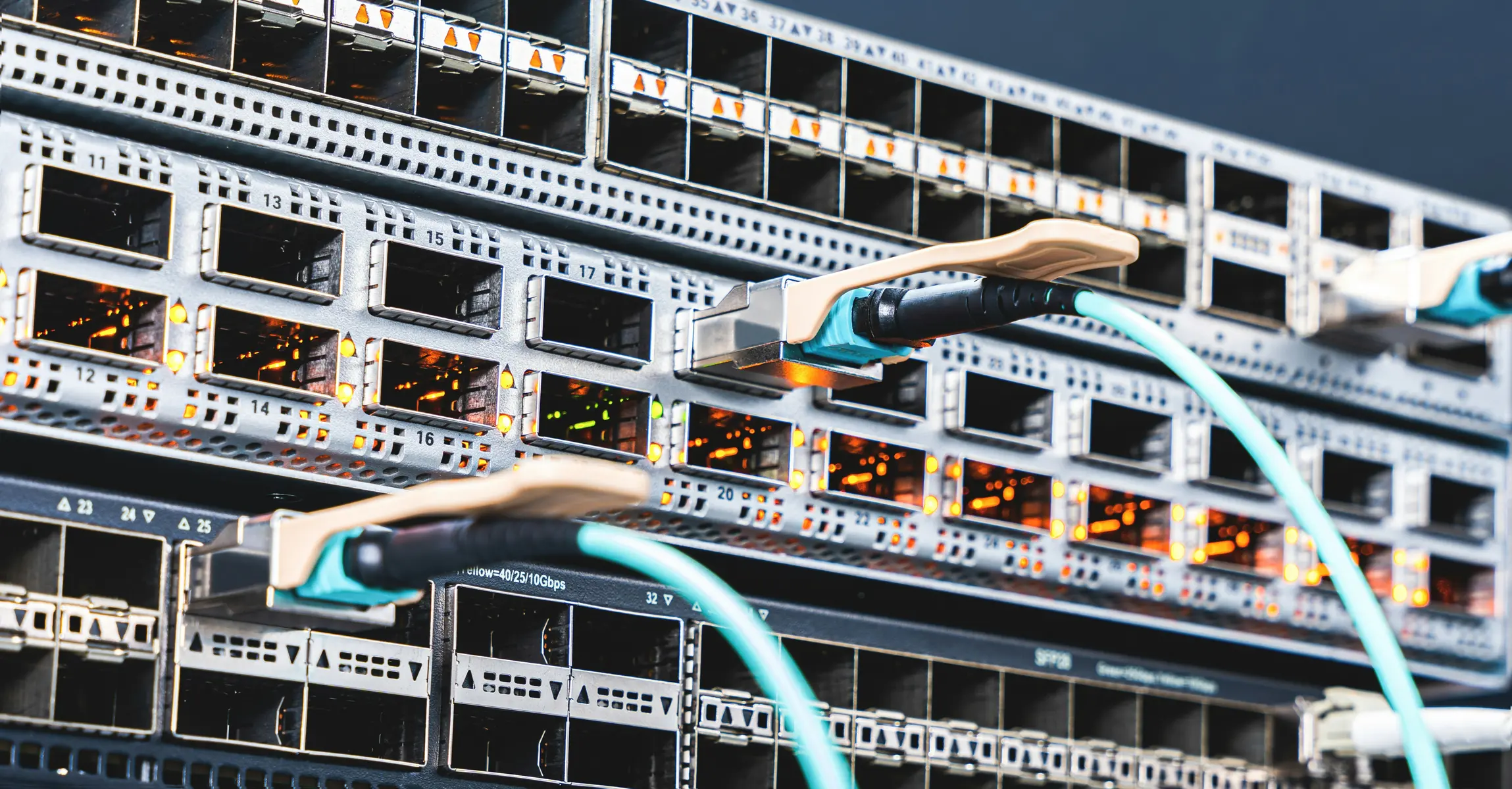 Nahaufnahme von Netzwerkswitches mit angeschlossenen Glasfaserkabeln in einem Rechenzentrum