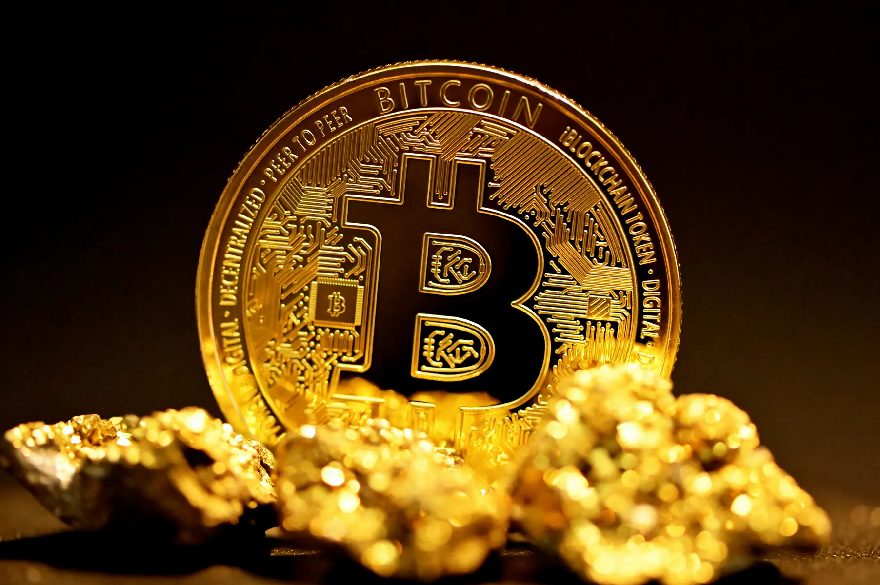 Eine goldene Bitcoin-Münze auf einem Haufen aus Goldnuggets vor schwarzem Hintergrund