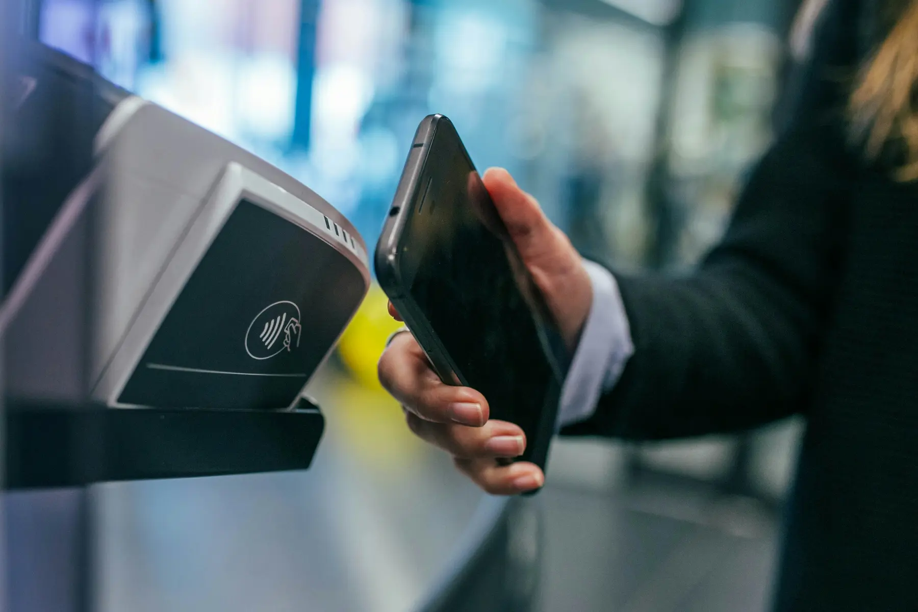 Eine Person hält ein Smartphone über ein kontaktloses Zahlungsgerät an einer Kasse