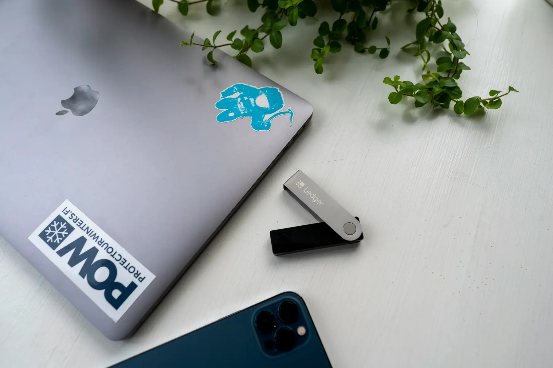 Eine Ledger Hardware-Wallet neben einem MacBook und einem Smartphone auf einem weißen Tisch.