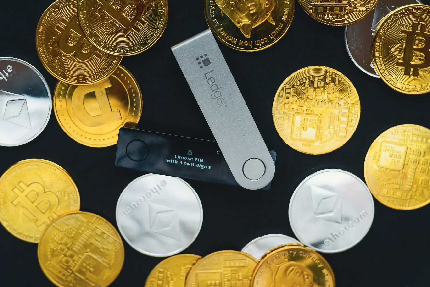 Eine Ledger Hardware-Wallet auf einem dunklen Hintergrund, umgeben von verschiedenen Kryptowährungs-Münzen.