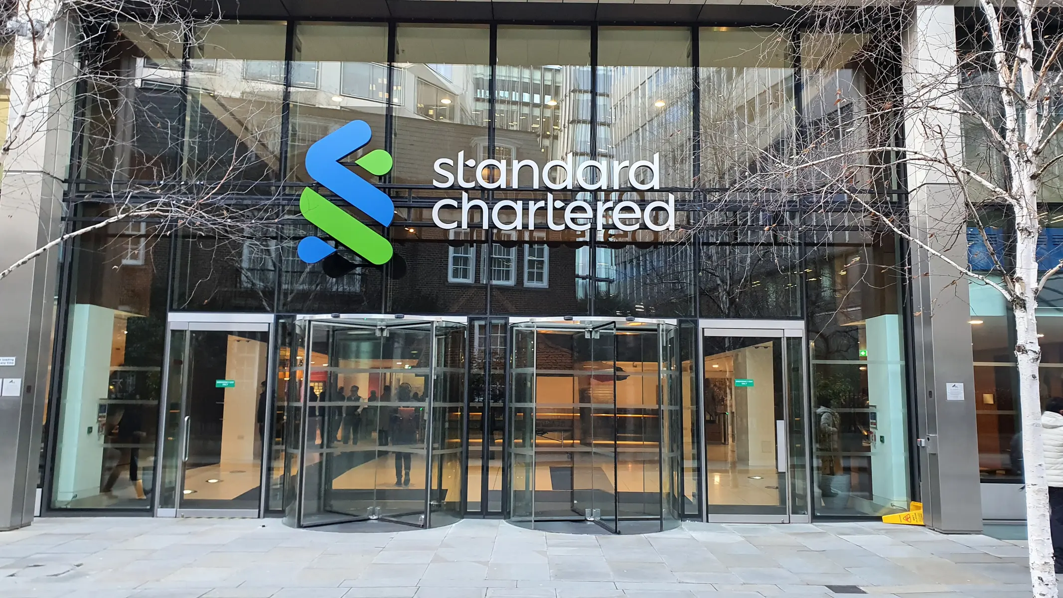 Die gläserne Fassade und der Eingang des Standard Chartered Hauptquartiers in London mit dem Firmenlogo.