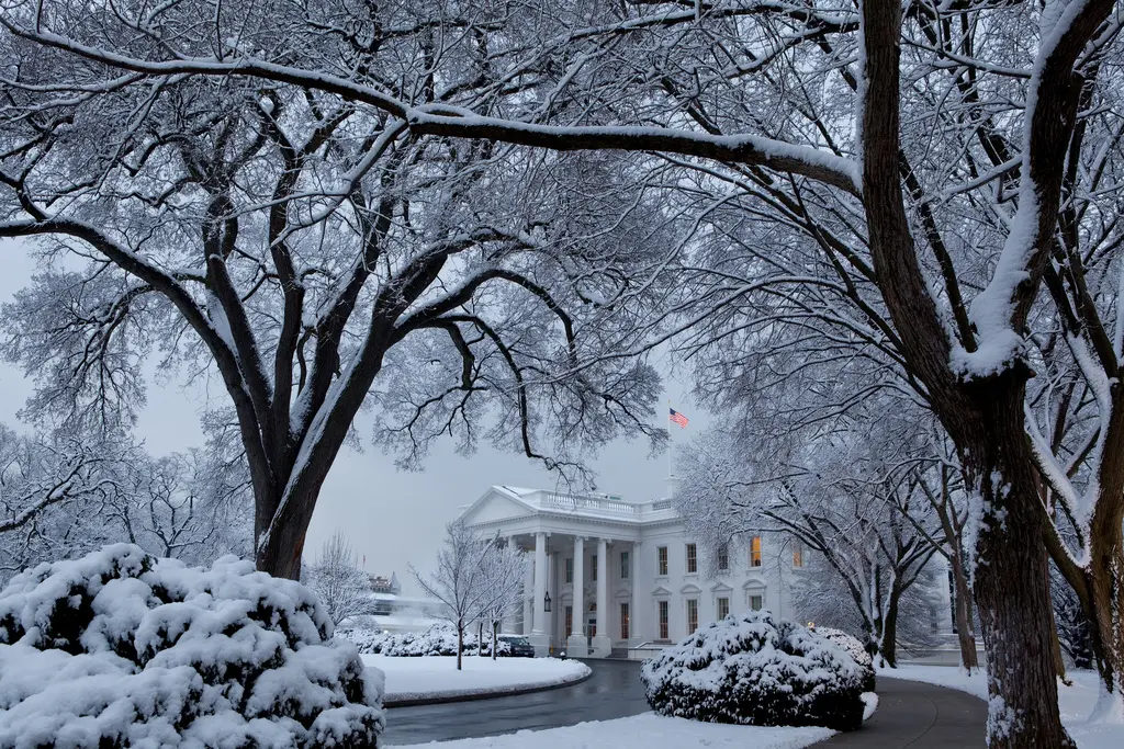 Das Weiße Haus in Washington, D.C., bedeckt mit einer Schneeschicht unter verschneiten Bäumen.