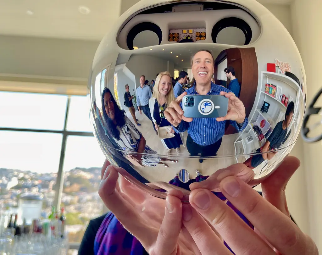 Eine Person hält den silbernen, kugelförmigen Worldcoin Orb, in dessen Oberfläche sich Menschen spiegeln.