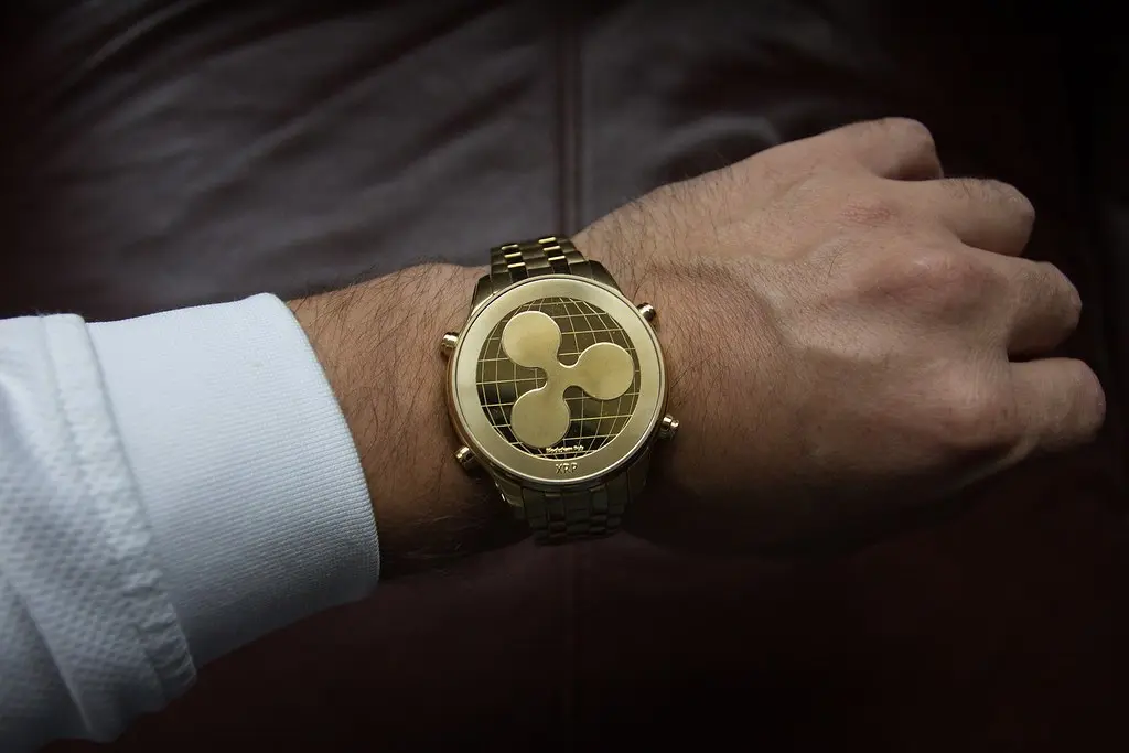 Eine goldene Armbanduhr mit dem XRP-Logo auf dem Zifferblatt an einem Handgelenk.