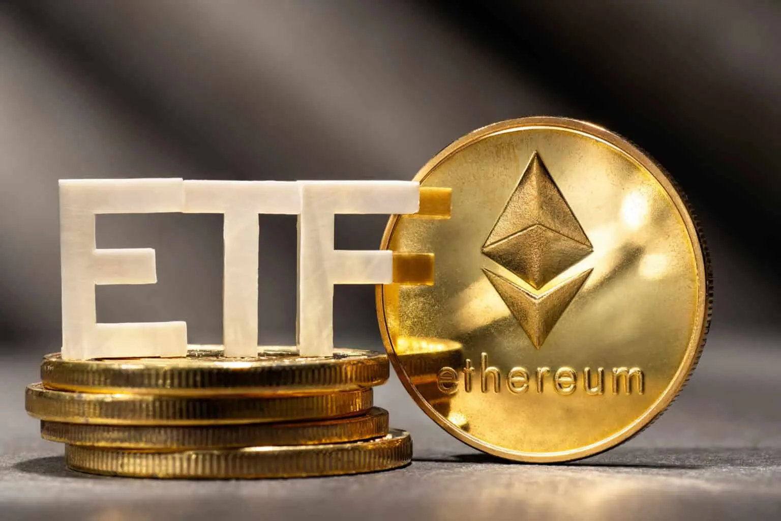 A gold Ethereum coin standing next to white 3D letters spelling ETF, atop a stack of gold coins