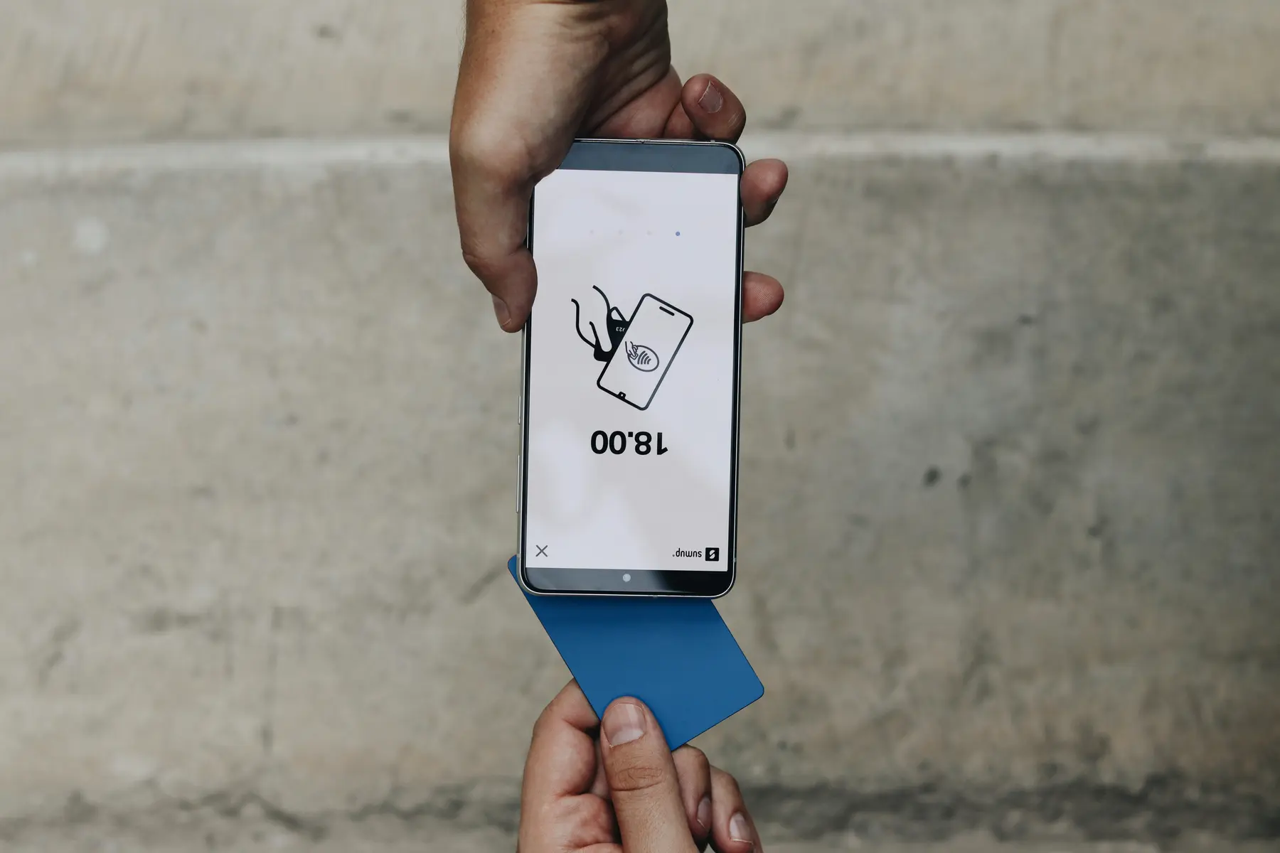 Een persoon die een blauwe betaalpas tegen een smartphone houdt voor een contactloze betaling.