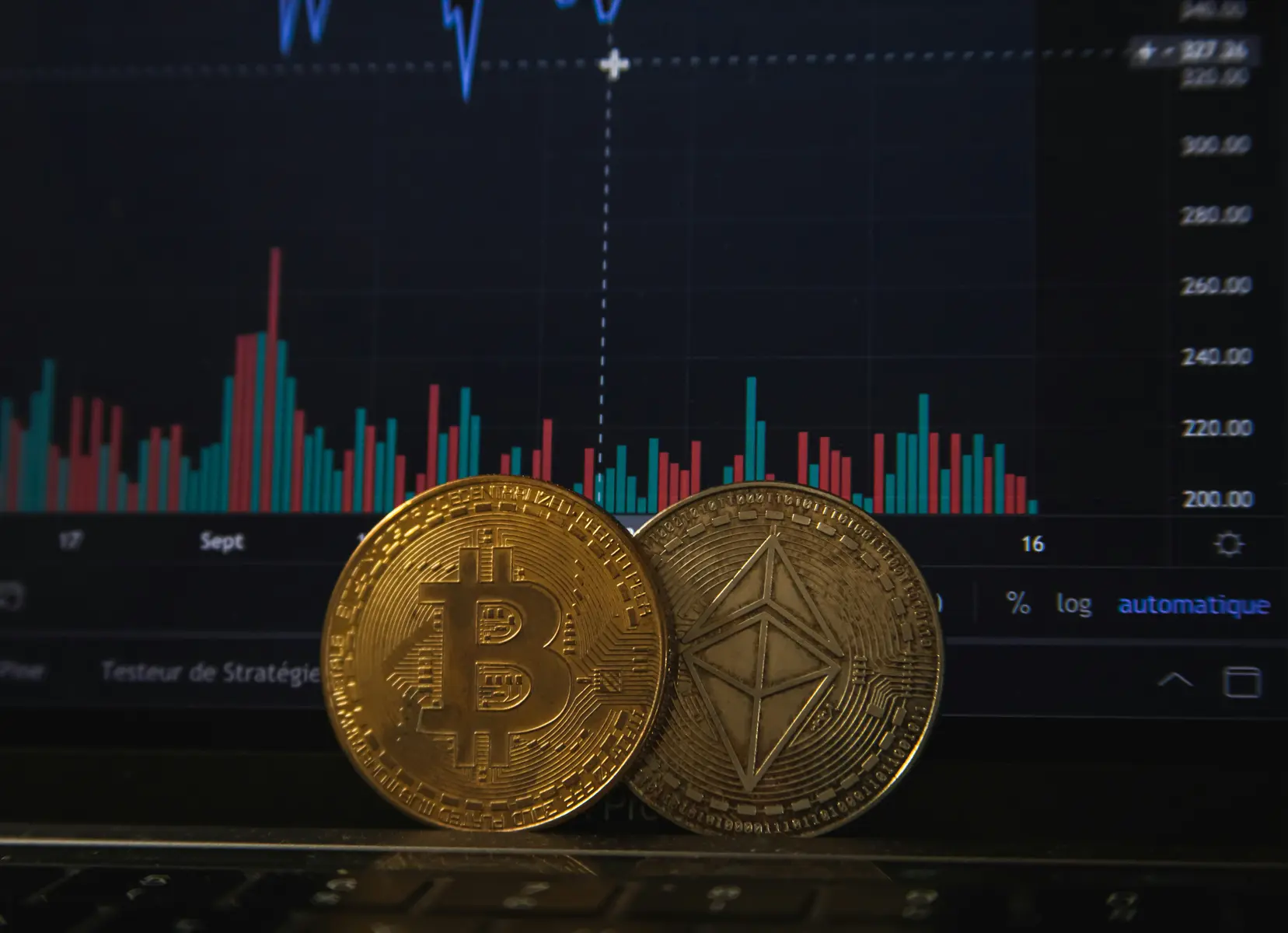 Bitcoin en Ethereum munten voor een laptop met een cryptohandelgrafiek.