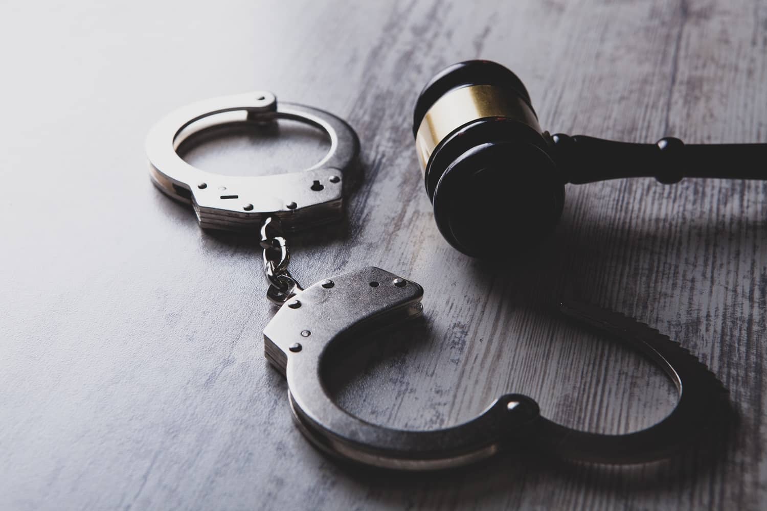 A judge’s gavel next to a set of handcuffs on a wooden table.