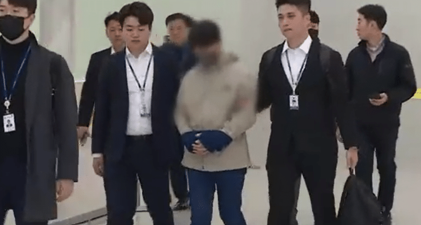 Choi, a man suspected of robbing a nursing care fund to buy cryptoassets, is escorted through an airport in South Korea.