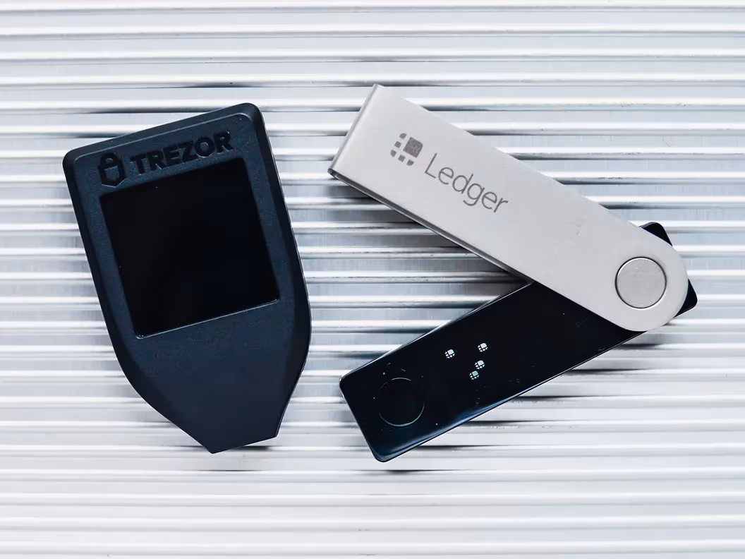 The image shows two popular hardware cryptocurrency wallets, a Trezor and a Ledger, used for securely storing digital assets offline.