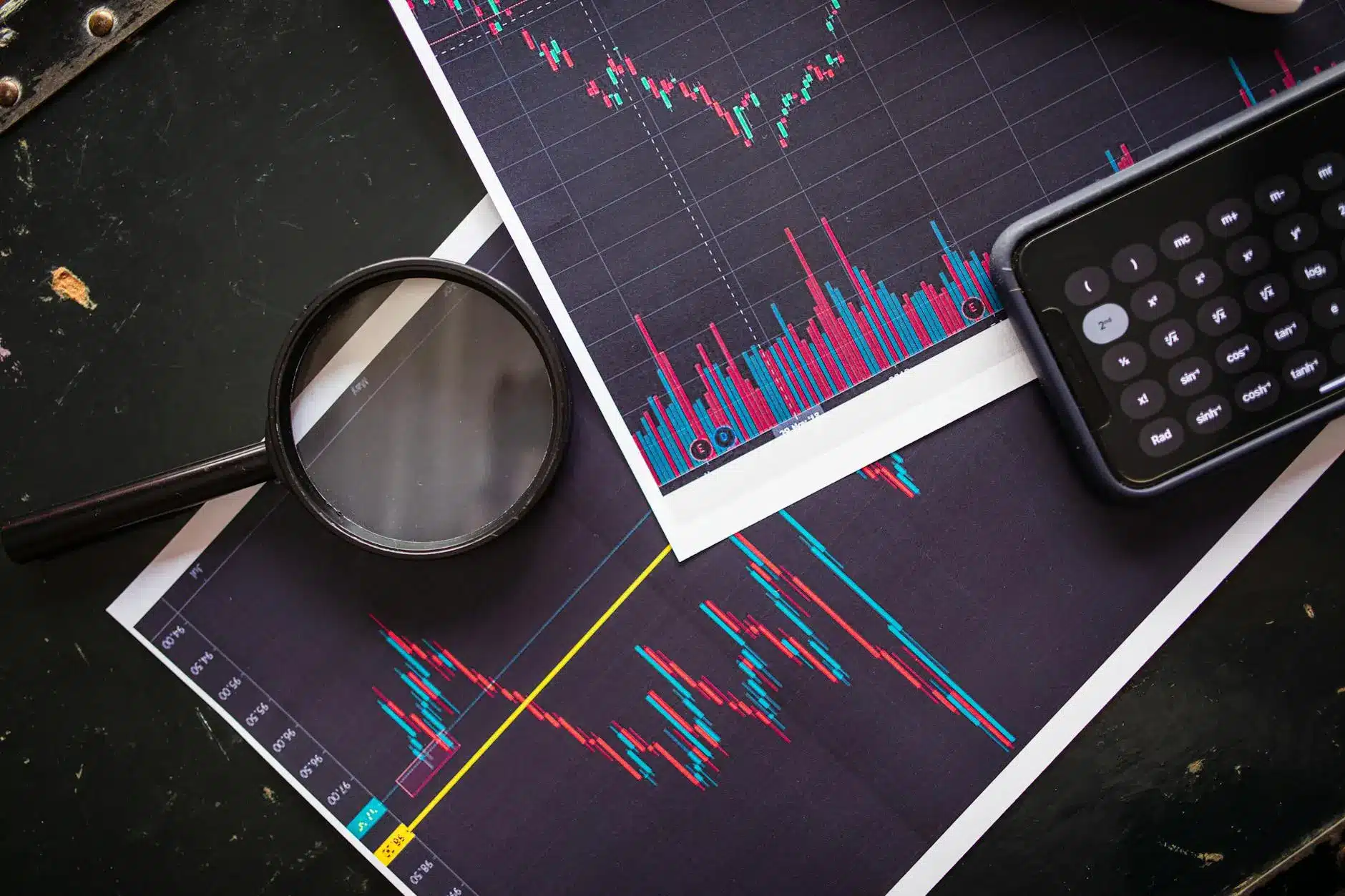 Chart analysis papers and a calculator on a dark surface, featuring financial data visuals.